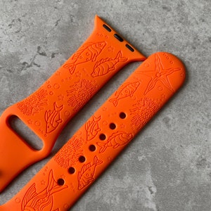 Puede incluir: Banda de reloj Apple de silicona naranja con un diseño de peces y corales.