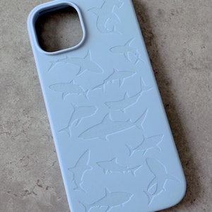 Puede incluir: Una funda de teléfono azul claro con un diseño en relieve de varios tiburones martillo.