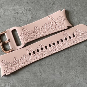 May include: A pink silicone watch band with a mushroom design. The band has a rose gold buckle.