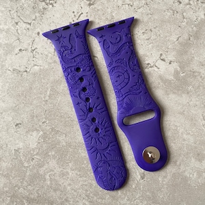 K&ouml;nnte beinhalten: Ein violettes Silikon-Uhrenarmband mit gepr&auml;gtem Muster aus Schlangen, Motten, Sonnen, Monden und Sternen. Das Armband besteht aus zwei Teilen, einem mit mehreren Einstelll&ouml;chern und einem mit einem silberfarbenen Metallstift-Verschlussmechanismus.