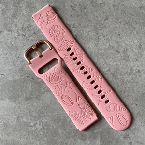 Op de afbeelding: Een roze siliconen horlogebandje met een gouden gesp. Het bandje is versierd met een schelpmotief.