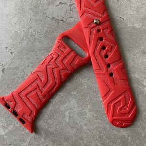 May include: Red silicone Apple Watch band with a geometric pattern.