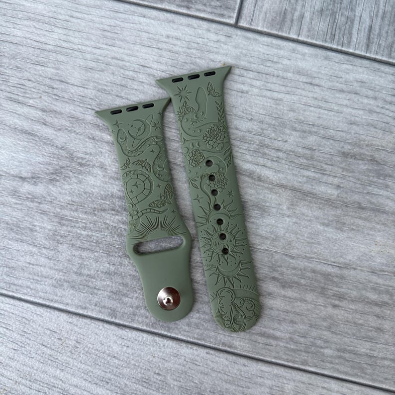 K&ouml;nnte beinhalten: Ein olivgr&uuml;nes Silikon-Uhrenarmband mit einem eingravierten Muster aus himmlischen Elementen wie Sonnen, Monden, Sternen, Schlangen und Motten. Das Armband besteht aus zwei Teilen mit einem Metallstiftverschluss und Standardanschl&uuml;ssen.