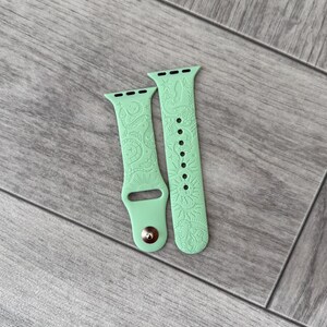 K&ouml;nnte beinhalten: Ein helles mintgr&uuml;nes Silikon-Uhrenarmband mit einem gepr&auml;gten Muster aus Schlangen, Sonnen, Monden, Sternen und einem Auge. Das zweiteilige Armband verf&uuml;gt &uuml;ber einen Metallstiftverschluss und mehrere L&ouml;cher zur individuellen Anpassung.