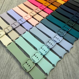 May include: A collection of colorful watch bands in various shades, including green, blue, pink, and orange. Each band features a buckle closure and is arranged in a diagonal pattern. The bands are made of a flexible material.