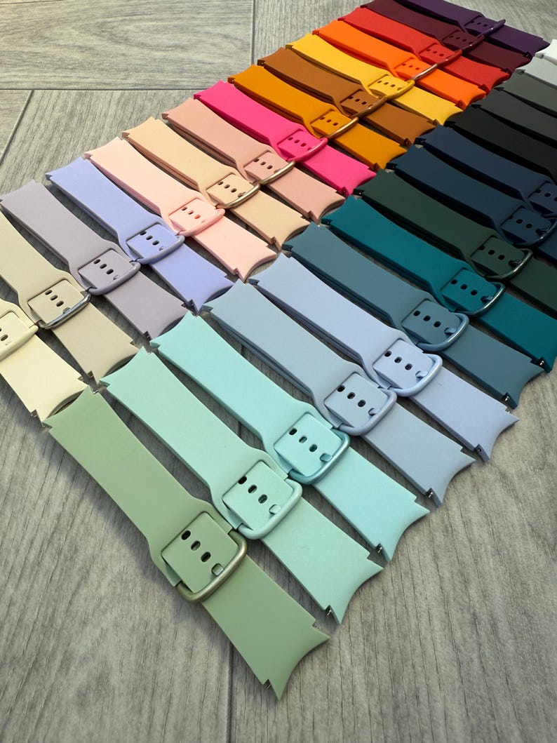 May include: A collection of colorful watch bands in various shades, including green, blue, pink, and orange. Each band features a buckle closure and is arranged in a diagonal pattern. The bands are made of a flexible material.