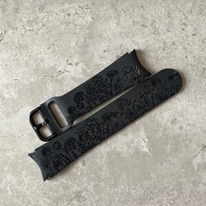 May include: Black silicone watch strap with a floral design. The strap is made of soft, flexible silicone and features a buckle fastening.