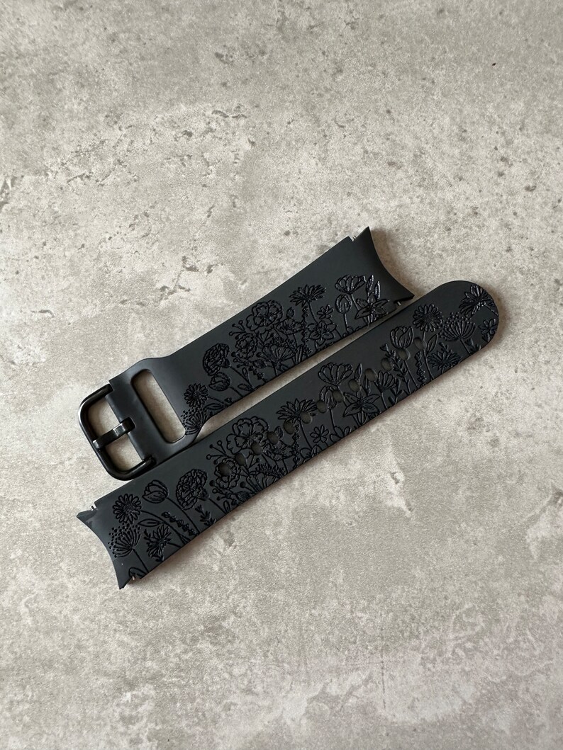 May include: Black silicone watch strap with a floral design. The strap is made of soft, flexible silicone and features a buckle fastening.