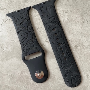 K&ouml;nnte beinhalten: Ein mattes, schwarzes Silikon-Uhrenarmband mit detaillierten Pr&auml;gemustern aus Schlangen, Motten, Sonnen, Monden und Sternen. Das zweiteilige Armband verf&uuml;gt &uuml;ber einen Metallstiftverschluss und Standard-Anschl&uuml;sse f&uuml;r die Uhr.