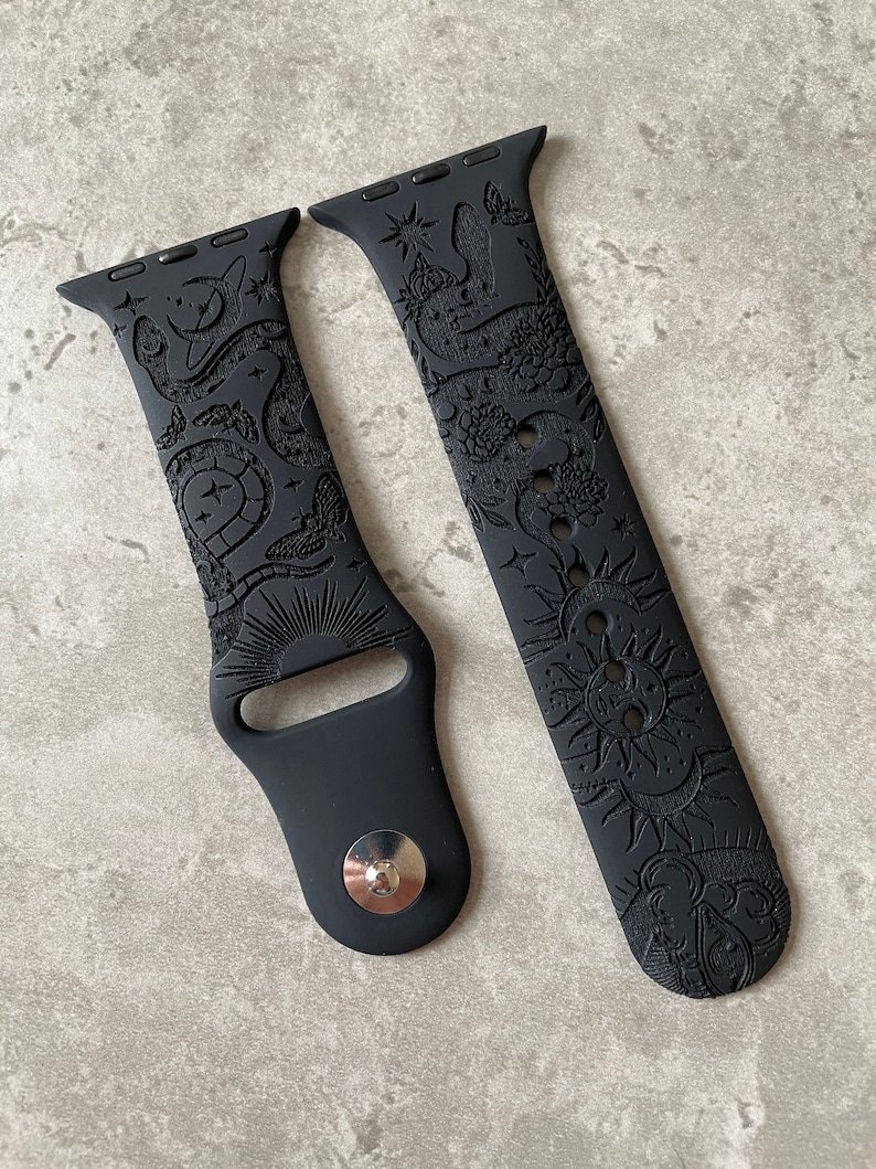 K&ouml;nnte beinhalten: Ein mattes, schwarzes Silikon-Uhrenarmband mit detaillierten Pr&auml;gemustern aus Schlangen, Motten, Sonnen, Monden und Sternen. Das zweiteilige Armband verf&uuml;gt &uuml;ber einen Metallstiftverschluss und Standard-Anschl&uuml;sse f&uuml;r die Uhr.