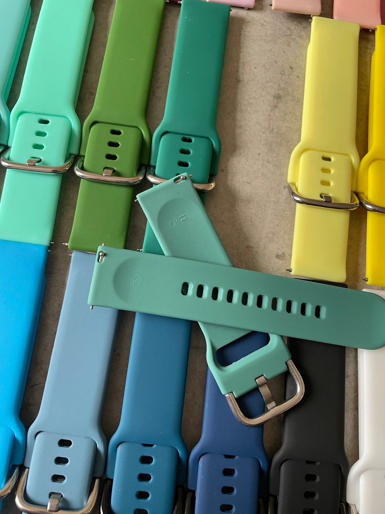 May include: Assortment of colorful silicone watch bands in various shades of blue, green, and yellow. The bands have a buckle closure and are designed for smartwatches.
