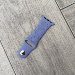 K&ouml;nnte beinhalten: Ein periwinkelfarbenes Uhrenarmband mit einem detaillierten Design von Meereskreaturen. Das Armband besteht aus einem flexiblen Material und verf&uuml;gt &uuml;ber einen silbernen Knopfverschluss. Das Design umfasst einen Oktopus und andere Meereslebewesen.
