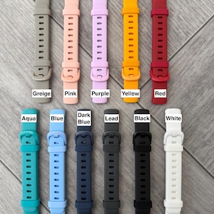 May include: Eleven silicone watch bands arranged in two rows, featuring colors labeled as Greige, Pink, Purple, Yellow, Red, Aqua, Blue, Dark Blue, Lead, Black, and White. Each band includes a matching buckle and multiple adjustment holes.