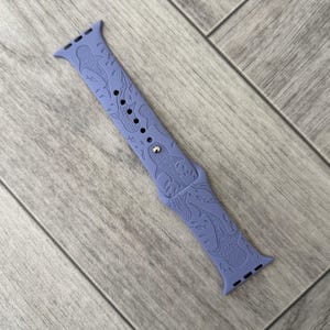 K&ouml;nnte beinhalten: Ein periwinkelfarbenes Uhrenarmband mit einem sich wiederholenden Muster aus Walhaien und anderen Meereslebewesen. Das Armband hat eine silberfarbene Schnalle und besteht aus einem flexiblen Material. Das Armband ist f&uuml;r eine Smartwatch konzipiert.