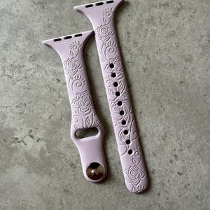 Puede incluir: Dos correas de reloj de silicona con un diseño floral en color morado claro. Las correas están diseñadas para Apple Watches.