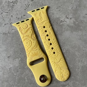 K&ouml;nnte beinhalten: Ein hellgelbes Silikon-Uhrenarmband mit gepr&auml;gtem Himmelsmotiv. Das Muster zeigt Sonne, Mond, Sterne, eine Schlange und Motten. Das Armband besteht aus zwei Teilen, wobei eines mit einem Metallstiftverschluss und das andere mit L&ouml;chern versehen ist.