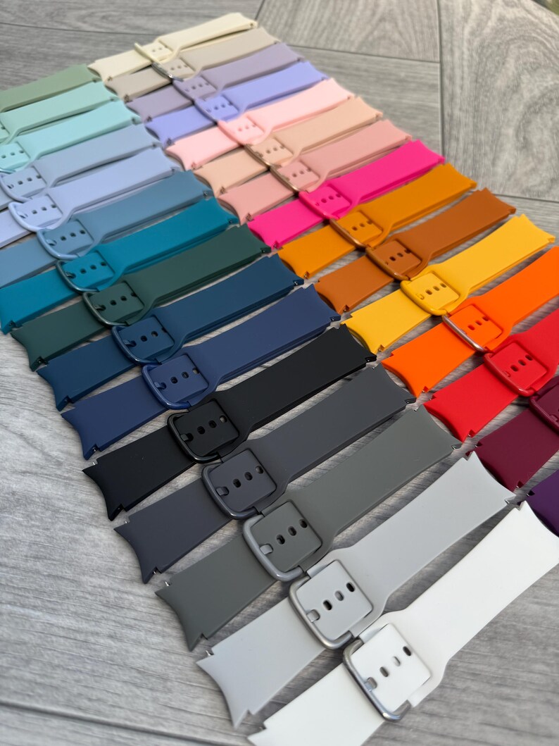May include: A collection of colorful watch bands in various shades, including blue, pink, orange, and gray. Each band features a buckle closure and is arranged in a diagonal pattern. The bands are made of a flexible material.