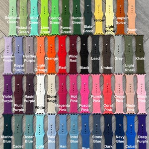 K&ouml;nnte beinhalten: Eine Sammlung farbenfroher, gravierter Uhrenarmb&auml;nder in verschiedenen Farbt&ouml;nen, darunter Gr&uuml;n, Lila, Rosa und Blau. Jedes Band ist mit einem dekorativen Muster graviert und mit seinem Farbnamen beschriftet. Die B&auml;nder sind in Reihen angeordnet und zeigen eine gro&szlig;e Auswahl.