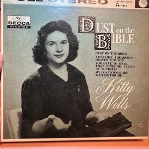 May include: Vintage vinyl record album cover for "Dust on the Bible" by Kitty Wells. The album cover features a black and white portrait of Kitty Wells, with the album title and song list in a decorative font. The Decca Records logo is visible.