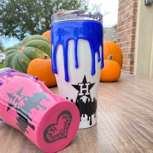 Puede incluir: Dos vasos aislados con base blanca y dise&ntilde;o de pintura goteada azul o rosa. Un vaso tiene un dise&ntilde;o de pintura goteada azul, y el otro tiene un dise&ntilde;o de pintura goteada rosa. Ambos vasos tienen un gr&aacute;fico negro de una estrella y un horizonte.