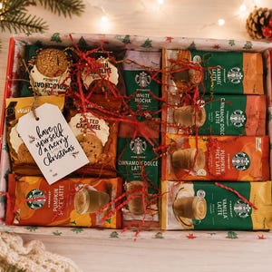 May include: A rectangular gift box filled with assorted Starbucks instant coffee sachets and Walkers biscuits. The box contains flavours like Caramel Latte, Pumpkin Spice Latte, and White Mocha, accented with red paper shreds and a white gift tag.