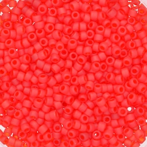 May include: A close-up image of a large quantity of small, opaque, red seed beads. The beads are round and have a slightly matte finish.