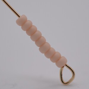 May include: A gold wire with a loop at the end strung with a series of light peach colored beads.