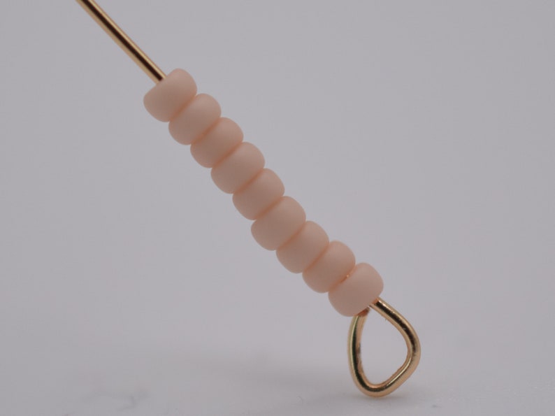 May include: A gold wire with a loop at the end strung with a series of light peach colored beads.