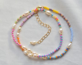 May include: A multi-strand necklace featuring colourful beads and white pearls. The necklace has a gold clasp and extender chain.
