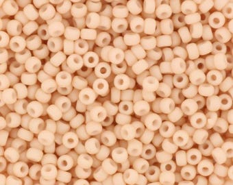 May include: A close-up view of a large quantity of small, round, opaque, peach-colored beads. The beads are all the same size and shape, and they are arranged in a random pattern.
