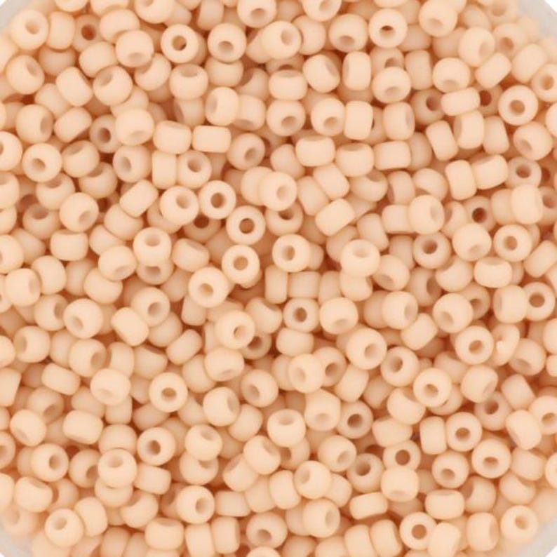 May include: A close-up view of a large quantity of small, round, opaque, peach-colored beads. The beads are all the same size and shape, and they are arranged in a random pattern.
