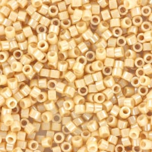 Puede incluir: Una imagen de primer plano de una gran cantidad de pequeñas cuentas redondas de color crema. Las cuentas tienen un agujero en el centro y están dispuestas en un patrón aleatorio.
