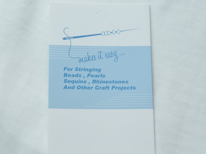 Może przedstawiać: Biała karta z niebieskim tekstem i niebieską ilustracją igły nawlekającej koraliki. Tekst brzmi "makes it easy... For Stringing Beads, Pearls Sequins, Rhinestones And Other Craft Projects".
