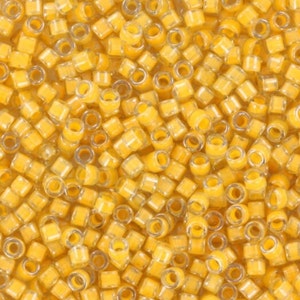 May include: A close-up image of a large quantity of small, square, transparent beads. The beads are a light yellow colour and have a glossy finish.