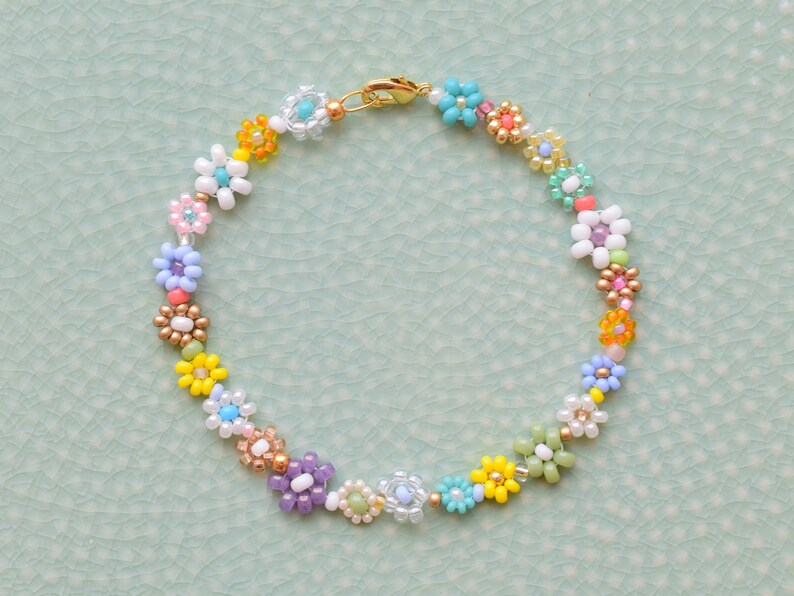 A bracelet made with seed beads of all colors and sizes. The beads are arranged in little flowers. Each flower is different and there is also a different bead between each flower. The clasp is gold.