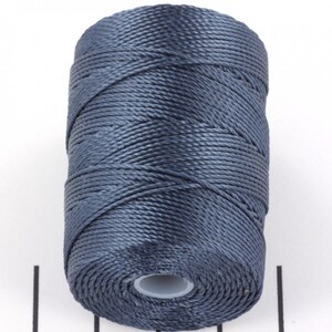May include: A dark blue thread spool, cylindrical in form, tightly wound. The thread appears to be a smooth, synthetic material, suitable for various craft projects. The spool is set against a white background, accentuating the thread's colour and texture.