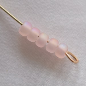 Pu&ograve; includere: Primo piano di una fila di perline rosa iridescenti infilate su un filo dorato con un anello di salto dorato all'estremit&agrave;.