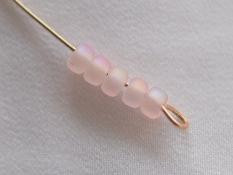 Pu&ograve; includere: Primo piano di una fila di perline rosa iridescenti infilate su un filo dorato con un anello di salto dorato all'estremit&agrave;.