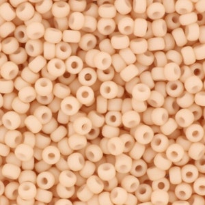 May include: A close-up image of a large quantity of small, round, opaque, peach-colored beads. The beads are all the same size and shape, and they are arranged in a random pattern.