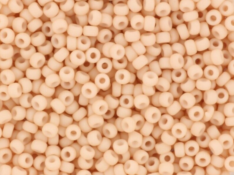 May include: A close-up image of a large quantity of small, round, opaque, peach-colored beads. The beads are all the same size and shape, and they are arranged in a random pattern.