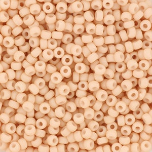 May include: A close-up view of a large quantity of small, round, opaque, light peach-colored beads.