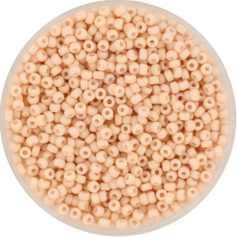 May include: A close-up view of a container filled with small, round, light peach-colored beads. The beads are arranged in a random pattern and appear to be made of glass or plastic.