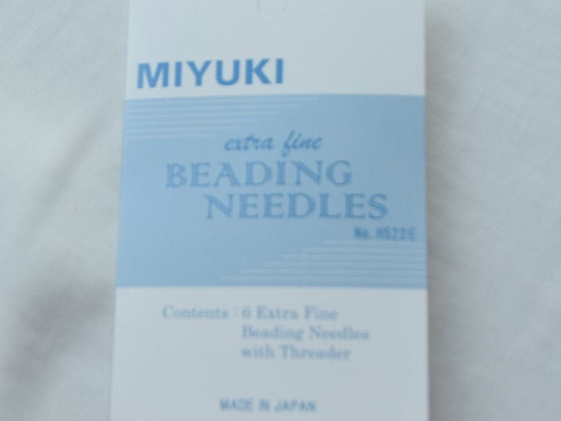 Może przedstawiać: Niebiesko-białe opakowanie igieł do koralik&oacute;w Miyuki extra fine. Opakowanie zawiera 6 igieł z nawlekaczem. Opakowanie jest oznaczone "Miyuki extra fine Beading Needles No. 5226" i "Made in Japan".