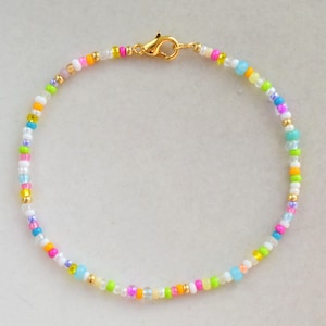 Peut inclure: Un bracelet en perles colorées avec un fermoir doré. Les perles sont de différentes nuances de rose, bleu, vert, jaune et blanc.