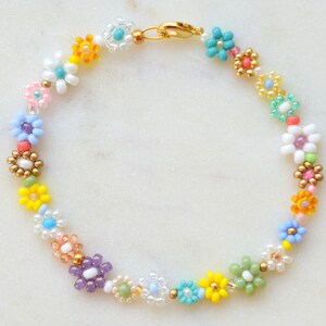 A bracelet made with seed beads of all colors and sizes. The beads are arranged in little flowers. Each flower is different and there is also a different bead between each flower. The clasp is gold.