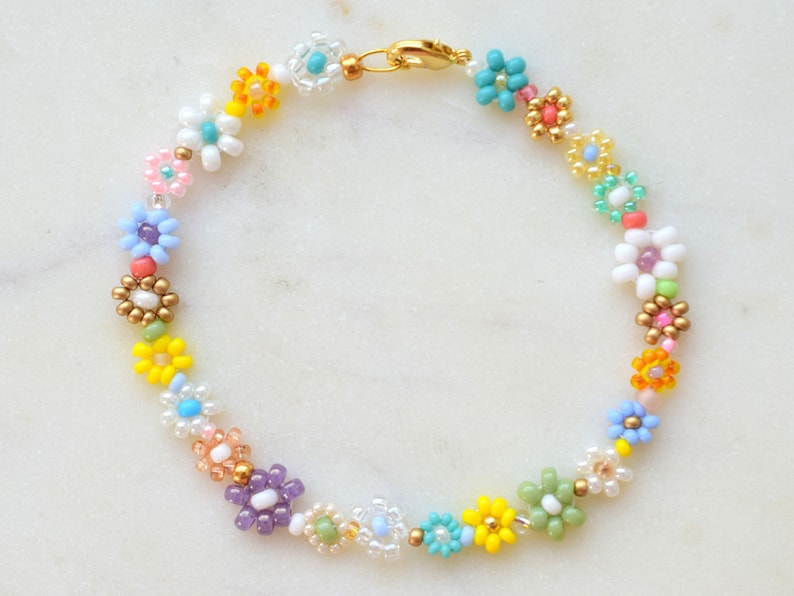 A bracelet made with seed beads of all colors and sizes. The beads are arranged in little flowers. Each flower is different and there is also a different bead between each flower. The clasp is gold.