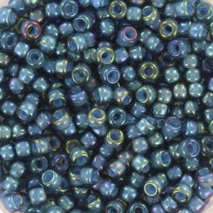 Könnte beinhalten: Nahaufnahme eines Haufens kleiner, irisierender blauer Perlen. Die Perlen haben eine zylindrische Form mit einem Loch in der Mitte. Die Oberfläche der Perlen reflektiert eine Reihe von Farben, darunter Blau, Grün und Lila.