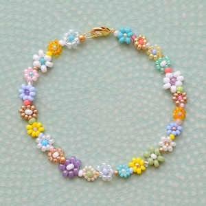 A bracelet made with seed beads of all colors and sizes. The beads are arranged in little flowers. Each flower is different and there is also a different bead between each flower. The clasp is gold.