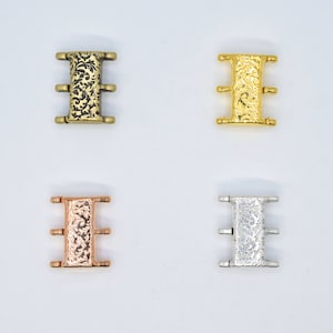 Op de afbeelding: Vier metalen connector-sluitingen in verschillende afwerkingen: antiek messing, goud, rosé goud en zilver. Elke sluiting heeft een decoratief bloemmotief en drie lussen.