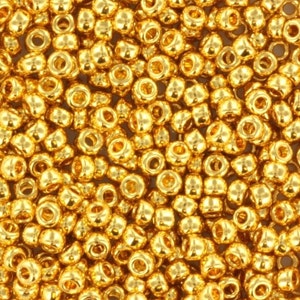 May include: A close-up image of a large quantity of small, round, gold-colored beads. The beads have a shiny, metallic finish.